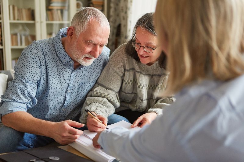 Senioren Paar unterschreibt ein Papier in Anwesenheit einer dritten Person.